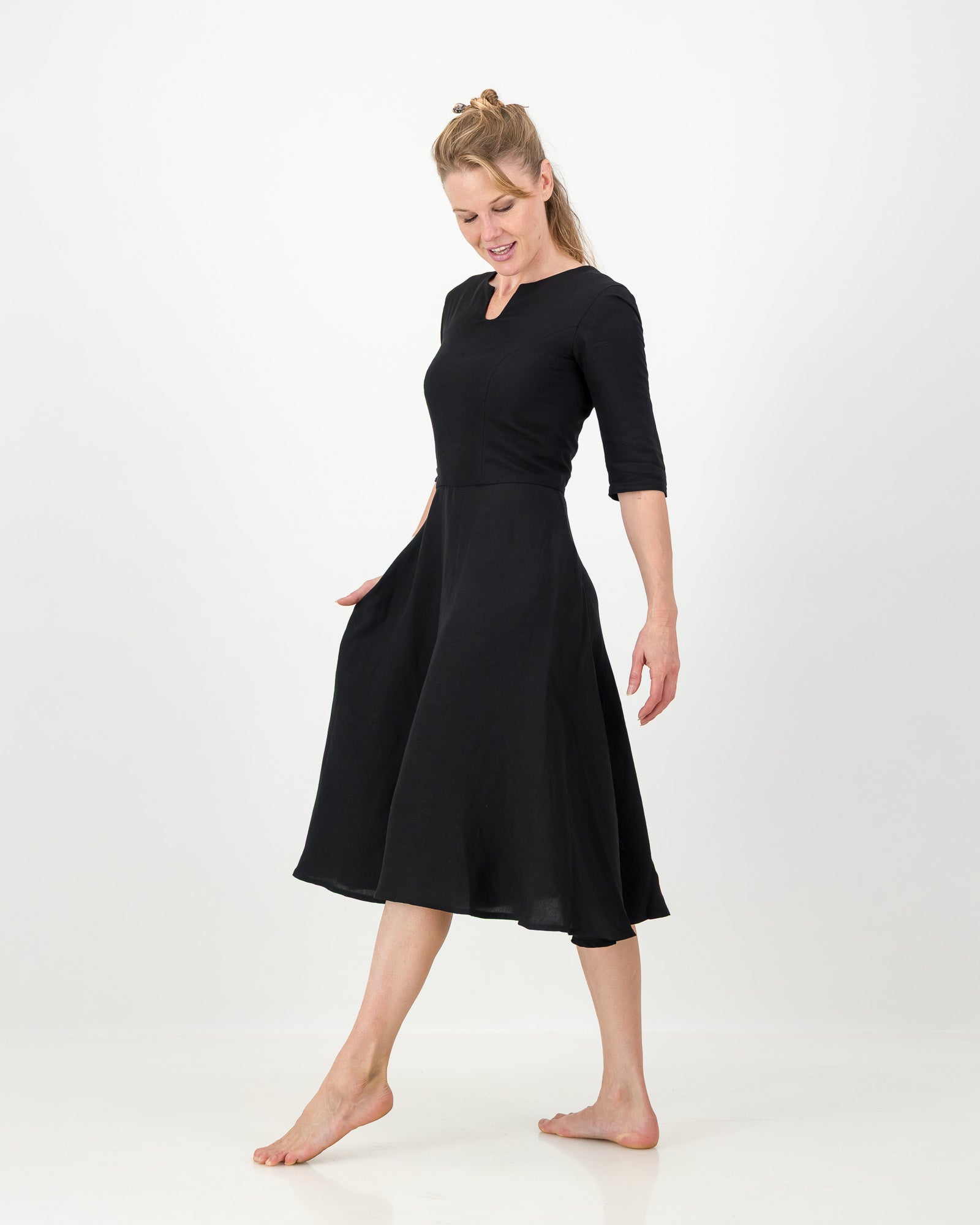 Woman wearing a black dress with fitted bodice and soft flared skirt with fitted elbow length sleeves and keyhole neckline on white background