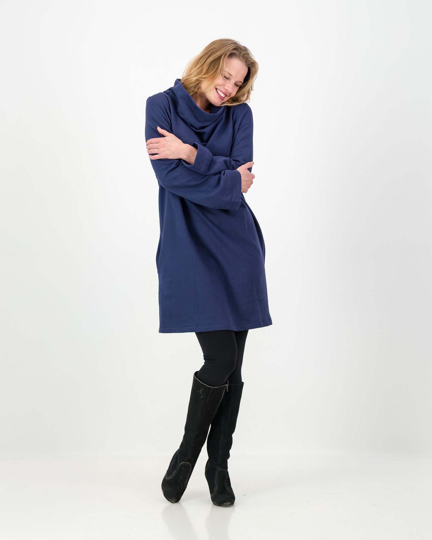 A navy-colored winter dress with a cowl neckline, full-length sleeves, and a straight cut, worn by a lady with black boots and leggings.