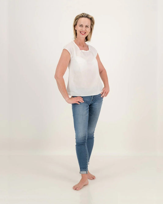 A woman wearing jeans and a twist on the classic white top. The top has a pleated neckline, adding elegance to its relaxed style. Stay cool and stylish in this lightweight cotton essential.