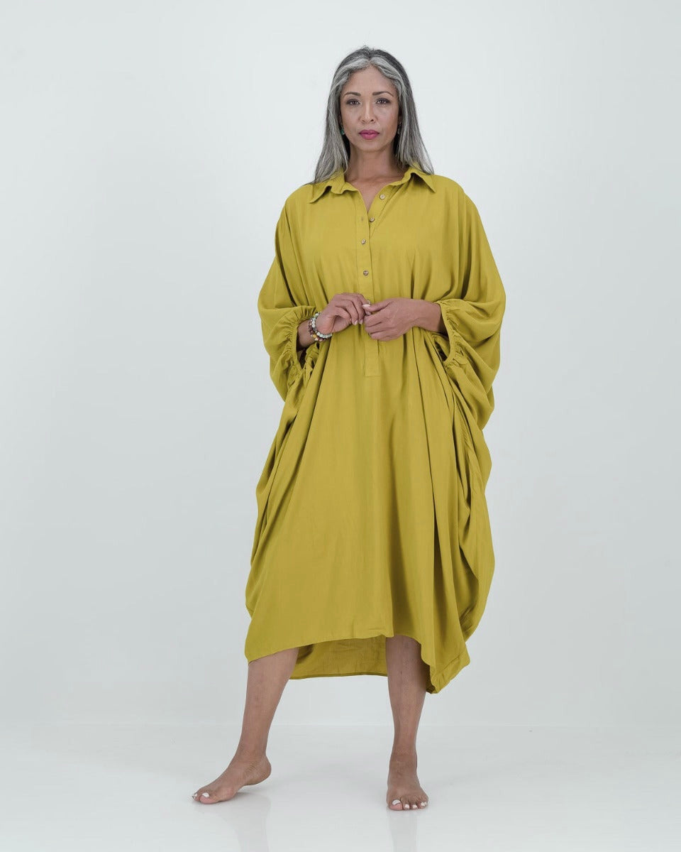 A model wearing a loose-fitting, lime-colored artist kaftan with a shirt collar and dramatic sleeves, featuring shell buttons and gathered cuff detailing.