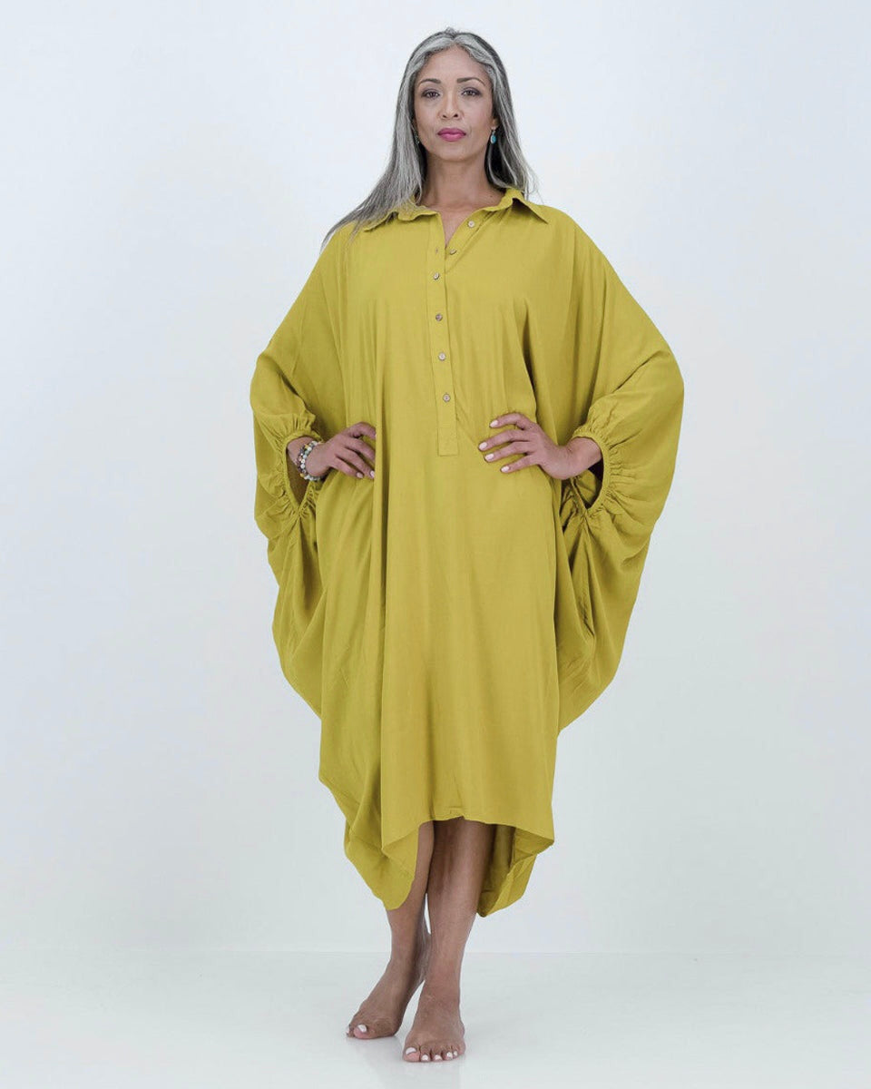 A model wearing a loose-fitting, lime-colored artist kaftan with a shirt collar and dramatic sleeves, featuring shell buttons and gathered cuff detailing.