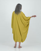 A model wearing a loose-fitting, lime-colored artist kaftan with a shirt collar and dramatic sleeves, featuring shell buttons and gathered cuff detailing.