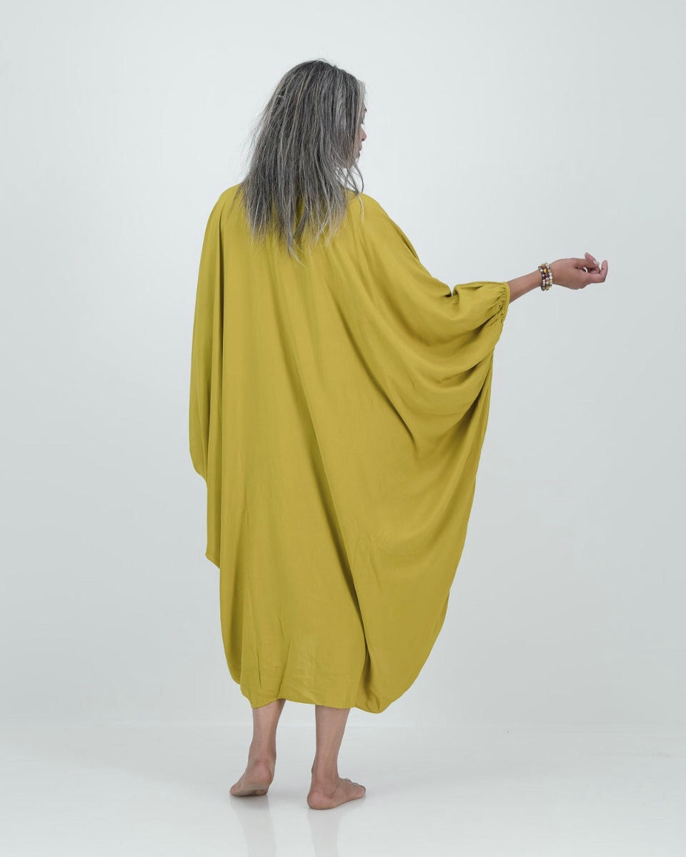 A model wearing a loose-fitting, lime-colored artist kaftan with a shirt collar and dramatic sleeves, featuring shell buttons and gathered cuff detailing.