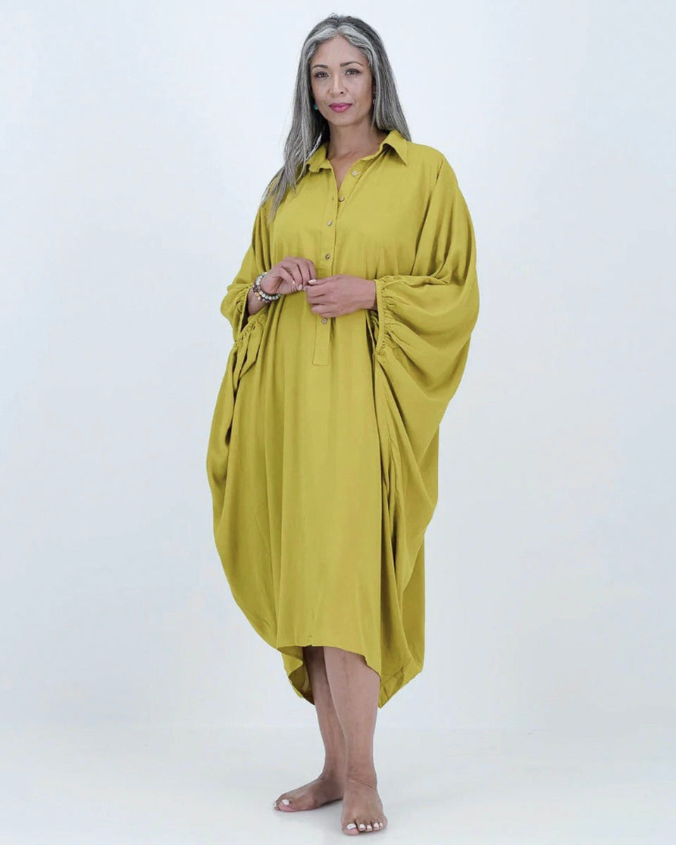 A model wearing a loose-fitting, lime-colored artist kaftan with a shirt collar and dramatic sleeves, featuring shell buttons and gathered cuff detailing.