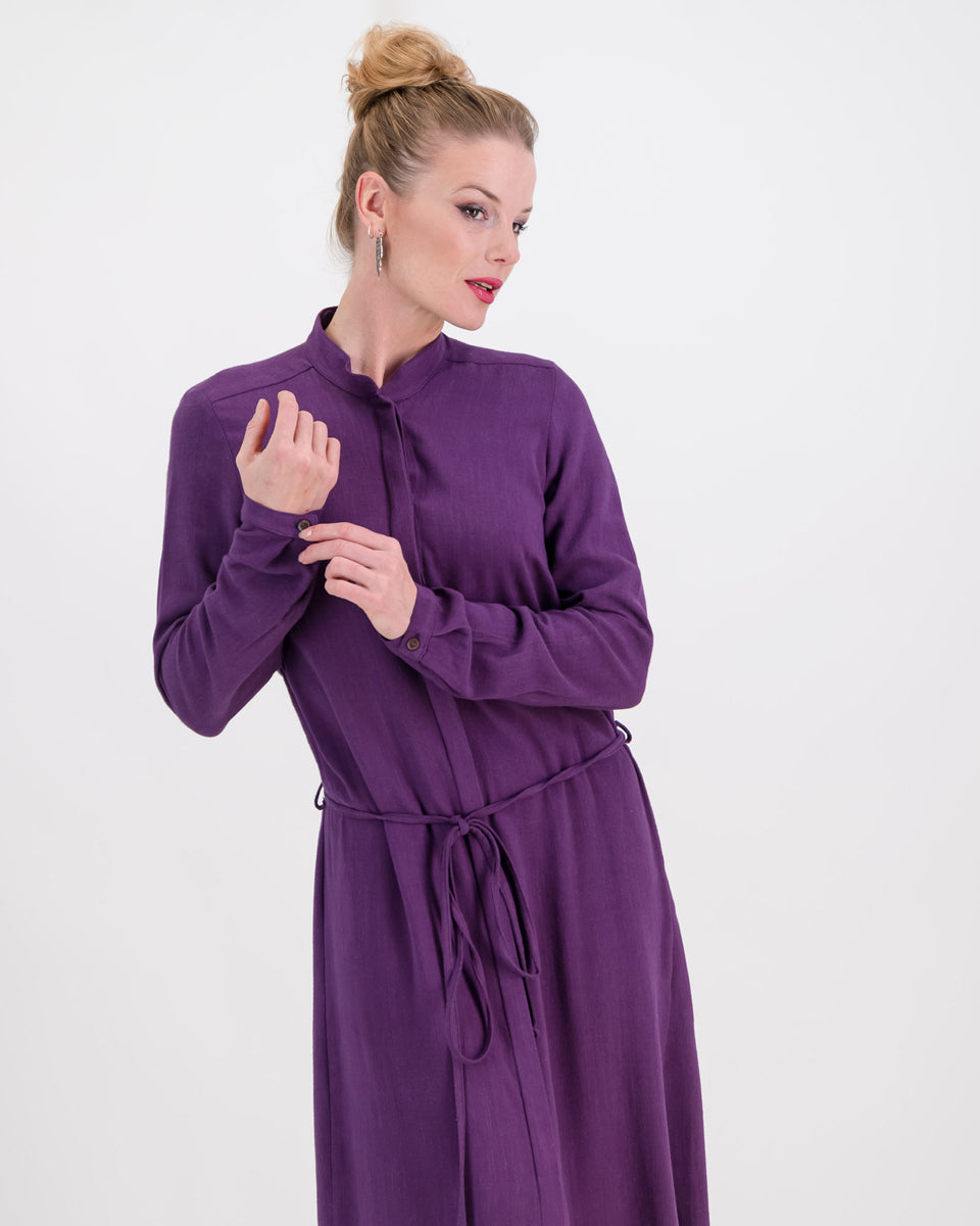 The deep purple imogen dress is shown here on a younger woman. She wears it effortlessly as the waist is cinched in with the built-in belt. The heavier linen/rayon blend fabric lets the dress fall beautifully and sits below the knee. The long sleeves of the dress can be worn ruched up or down depending on the weather.