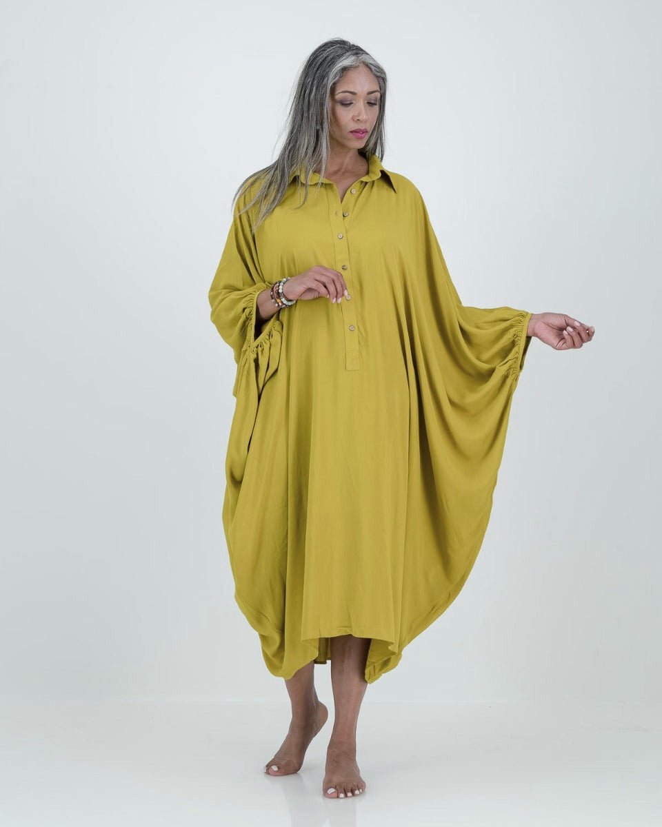 A model wearing a loose-fitting, lime-colored artist kaftan with a shirt collar and dramatic sleeves, featuring shell buttons and gathered cuff detailing.