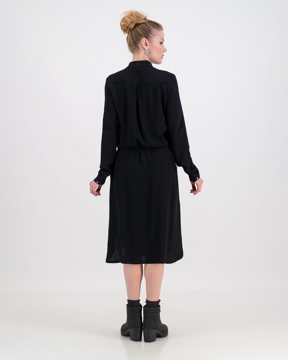 The back of the imogen dress is depicted in this image. A vibrant women stands with her back facing us. The dress is below knee length and the waist is cinched in with the built-in belt.