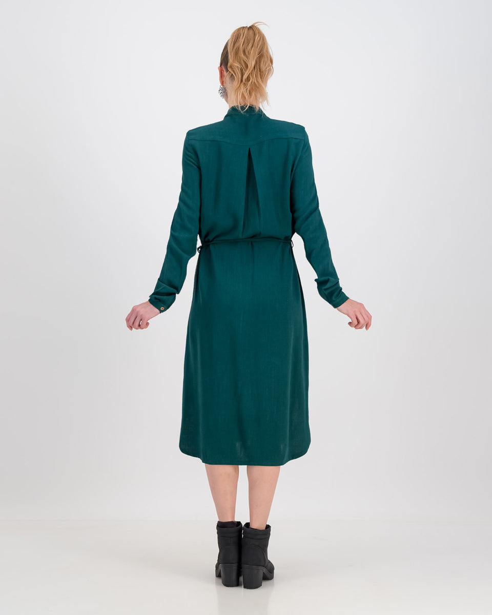 The back of the imogen dress is shown here. The emerald green imogen dress has a cinched waist and long sleeves that can be rolled or folded up. The below the knee hemline is flattering and elongating on the body. The dress also features a bak yolk for added movement and comfortability.