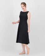 A model wearing a black sleeveless, boat neckline, fit and flare, knee-length dress with a center back zip.