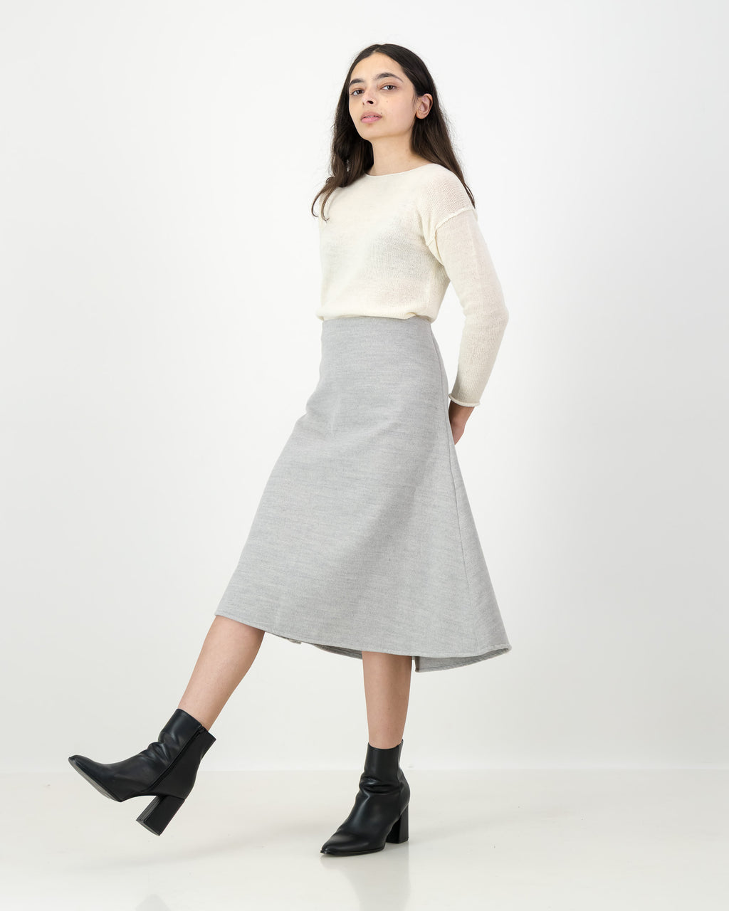 Woman wearing a cream sweater and gray skirt on a white background