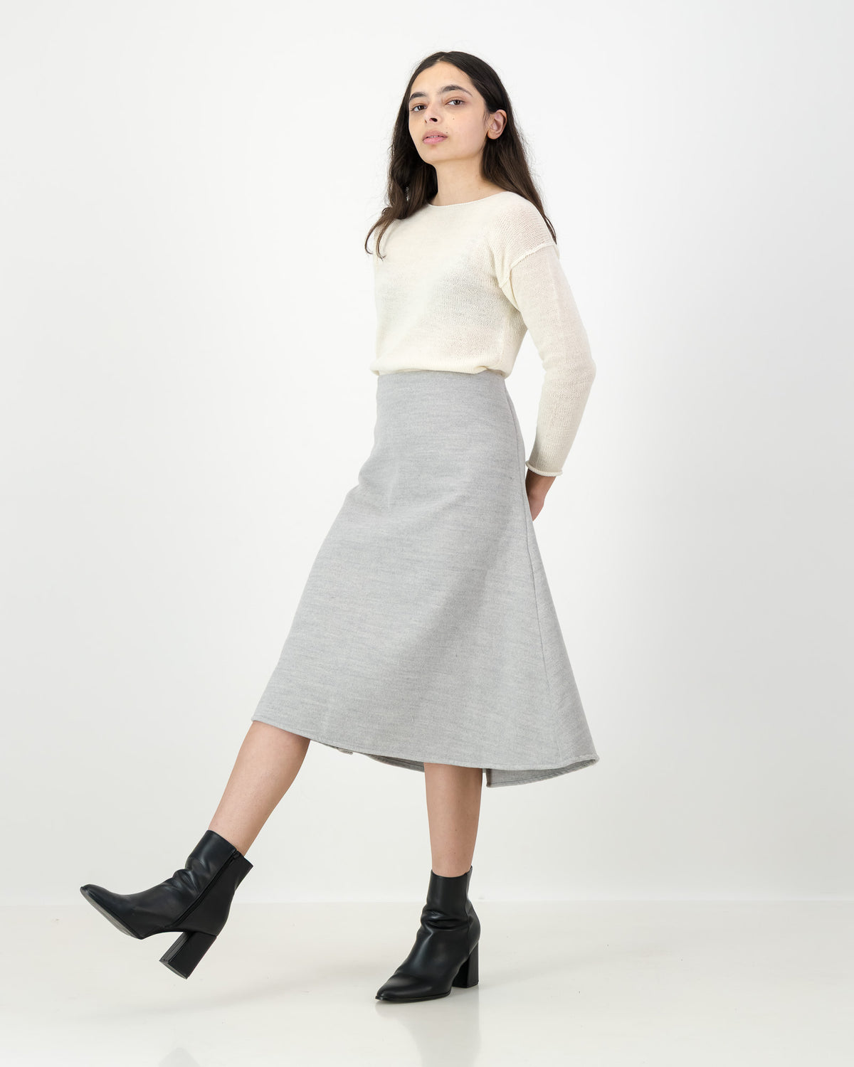 Woman wearing a cream sweater and gray skirt on a white background