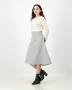 Woman wearing a cream sweater and gray skirt on a white background