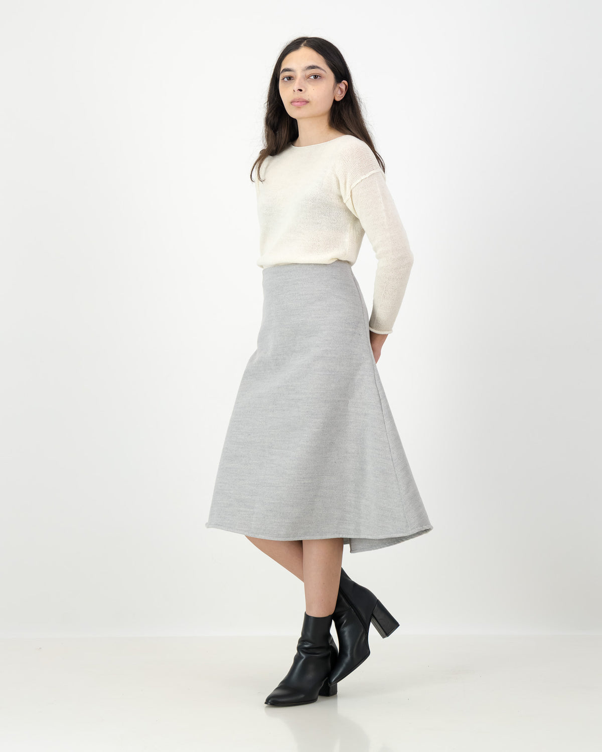 Woman wearing a cream sweater and gray skirt on a white background