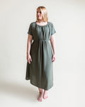 Woman wearing a green drawstring dress with short sleeve against a plain background