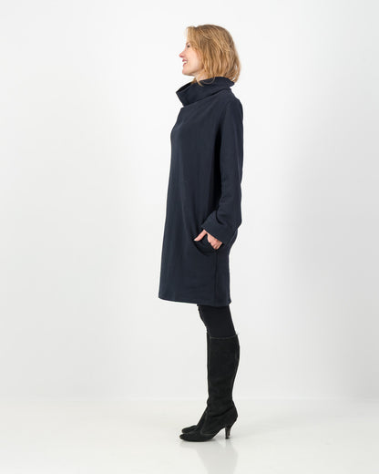 Side view of a black-colored winter dress with a cowl neckline, full-length sleeves, and a straight cut, worn by a lady with black boots and leggings.