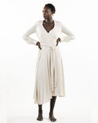 A model wearing a stone-colored eva wrap dress with a v-neckline, long sleeves, covered buttons, and an asymmetrical hem.