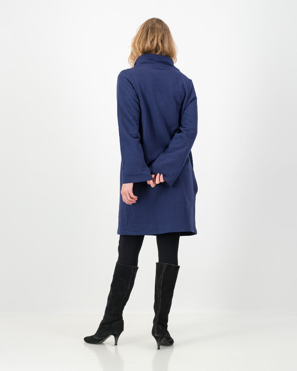 Back view of a navy-colored winter dress with a cowl neckline, full-length sleeves, and a straight cut, worn by a lady with black boots and leggings.