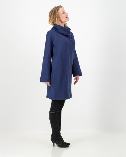 Side veiw of a navy-colored winter dress with a cowl neckline, full-length sleeves, and a straight cut, worn by a lady with black boots and leggings.