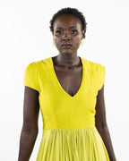 A woman models a chartreuse-colored knee-length dress with a gathered skirt and a V-neckline. The dress features cap sleeves and a flattering waist cinch.