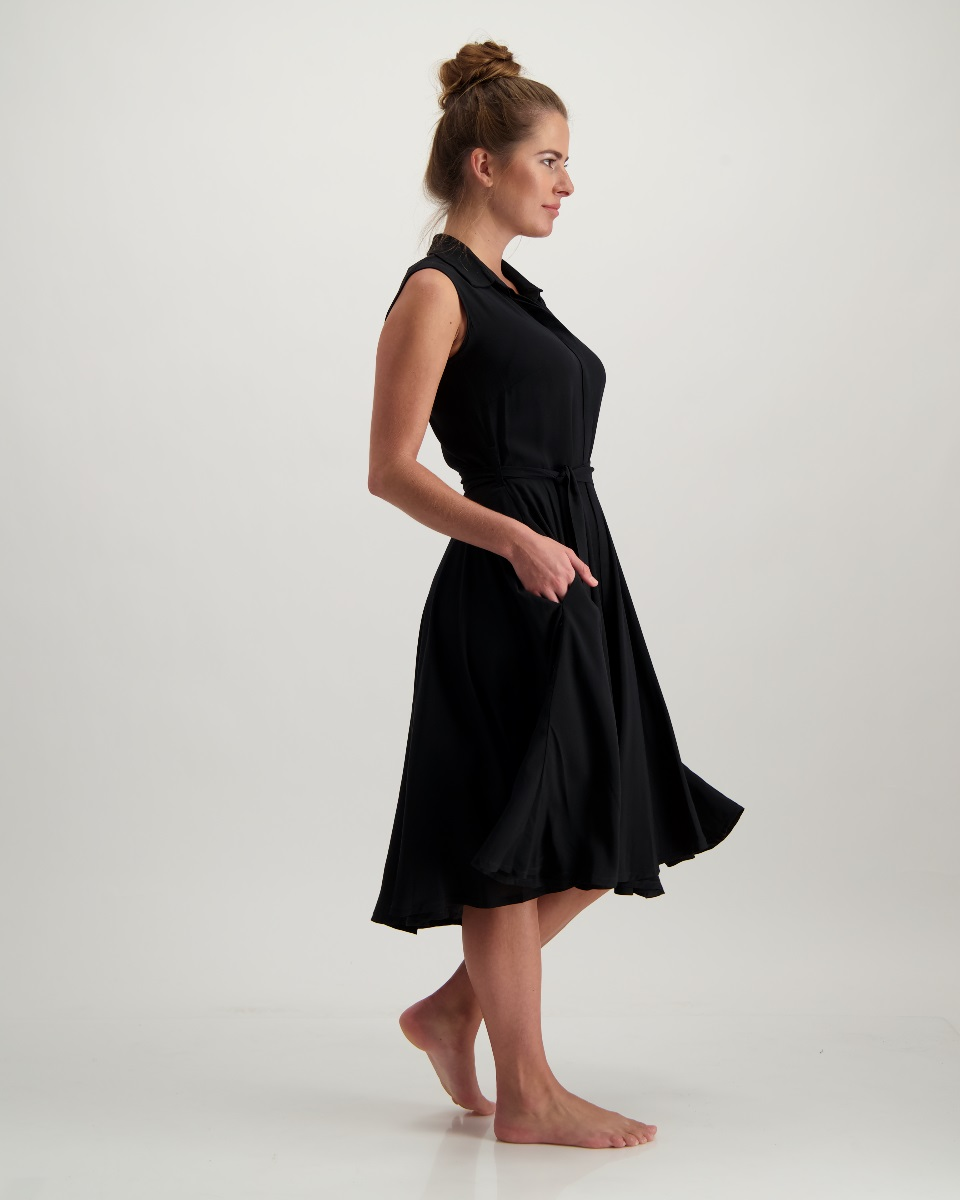 A poised woman in an elegant black dress, with a shirt collar, fitted waist, full circle skirt, and hidden button stand. 