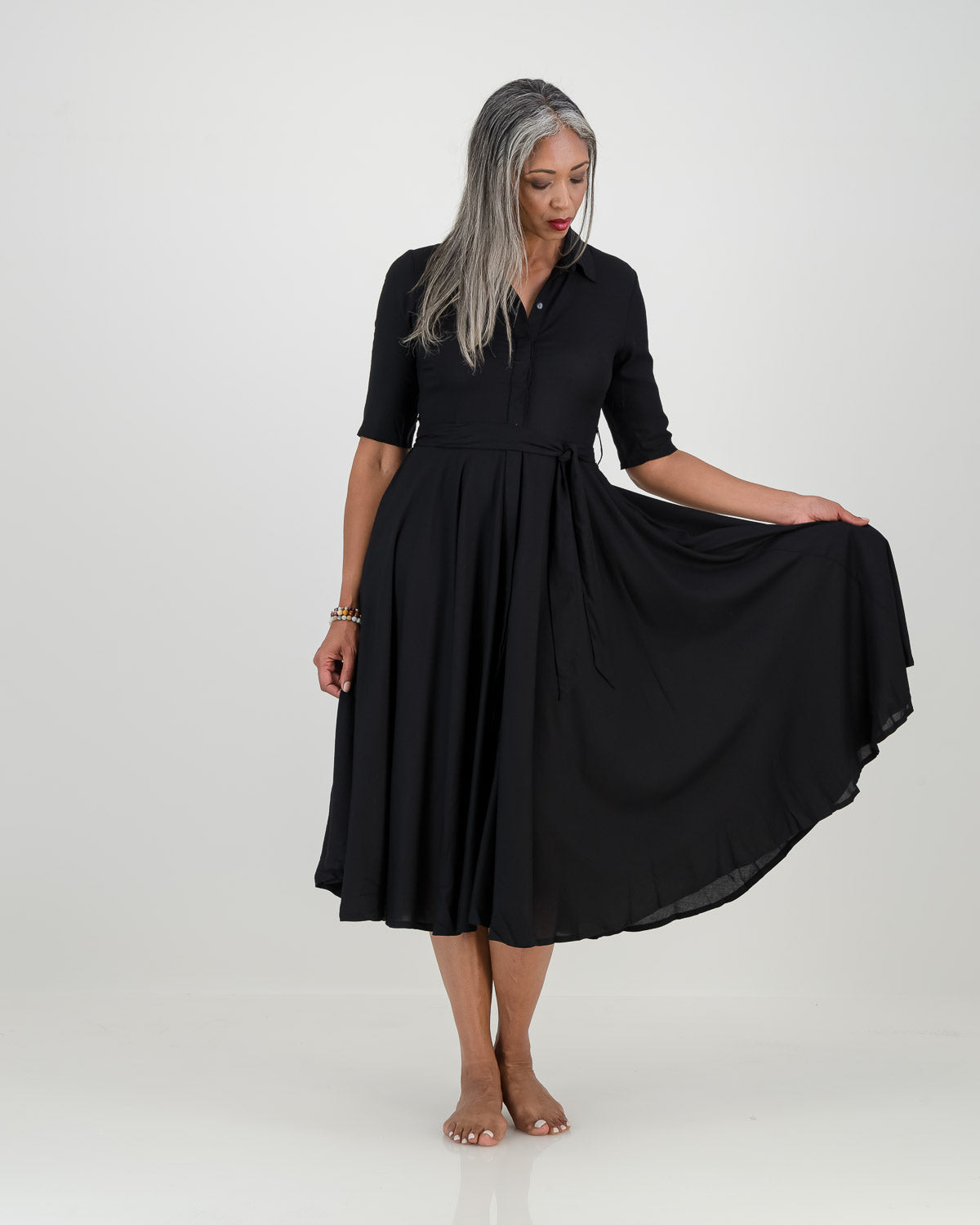 A woman in a black dress with 3/4 sleeves, collar, fitted waist, and full circle skirt. Versatile and elegant, perfect for any occasion!